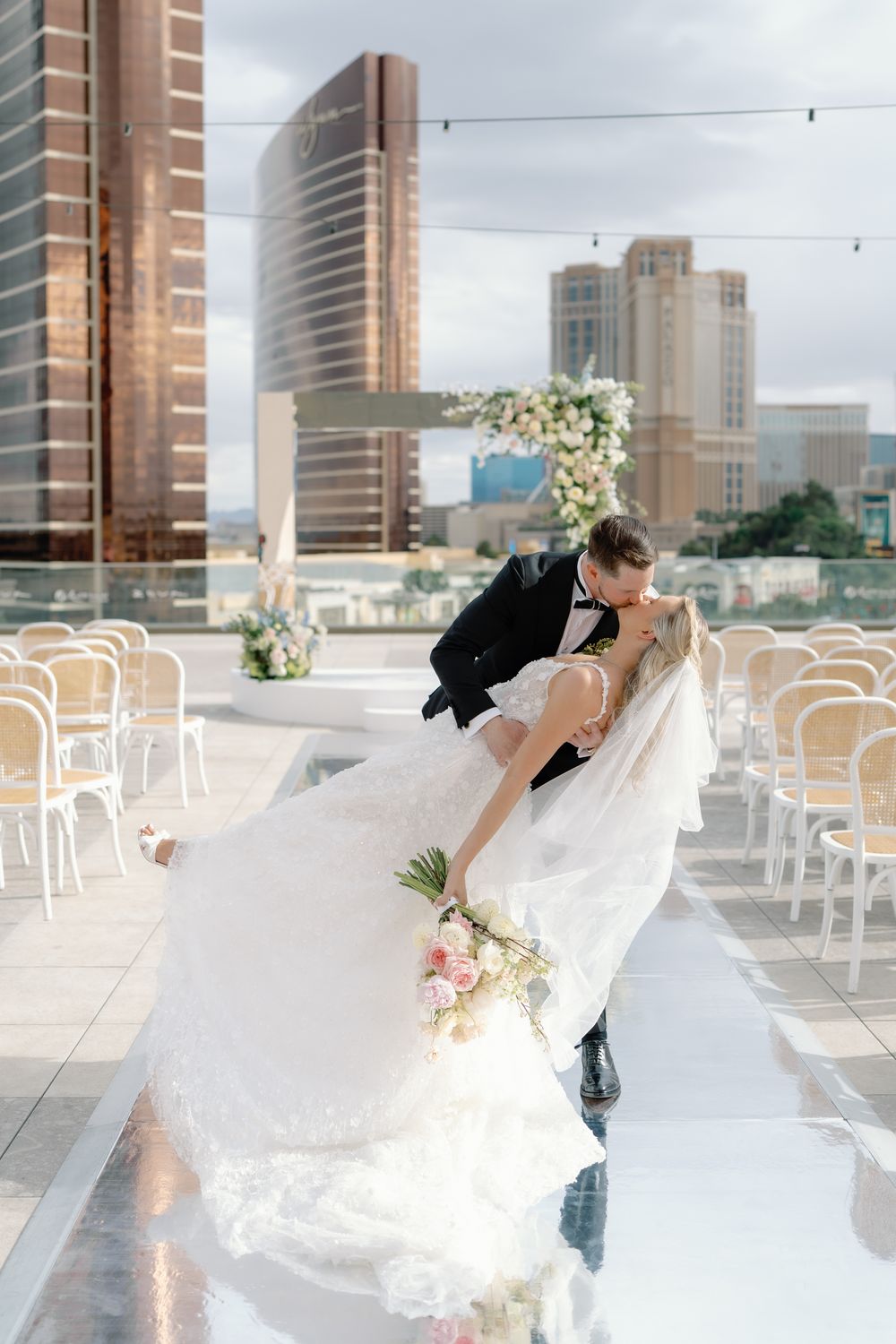 Bride and groom share romantic dip kiss on rooftop wedding venue with Las Vegas skyline in background.