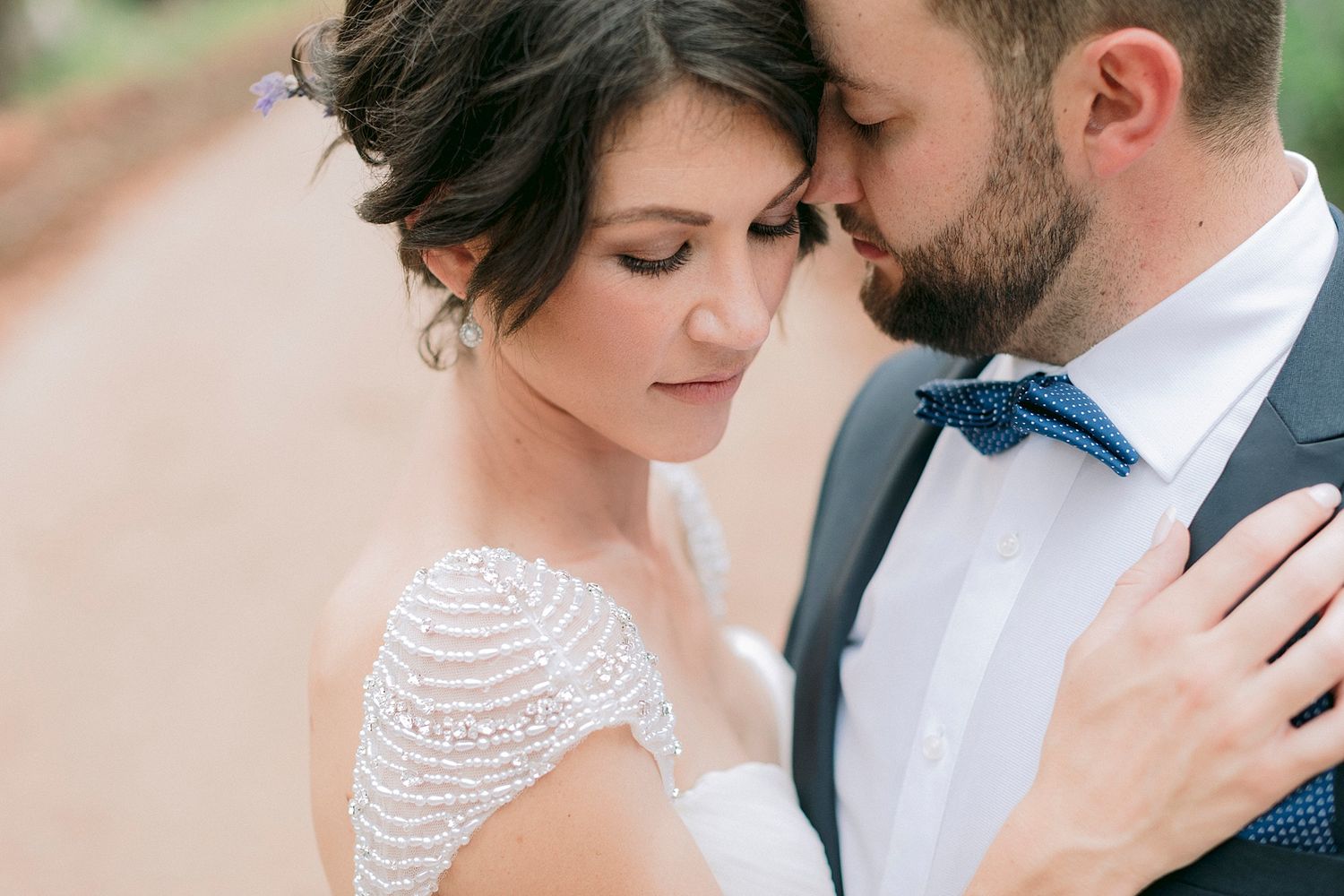 Elegant bride in off-shoulder lace wedding gown wrapped in flowing veil in soft natural light.