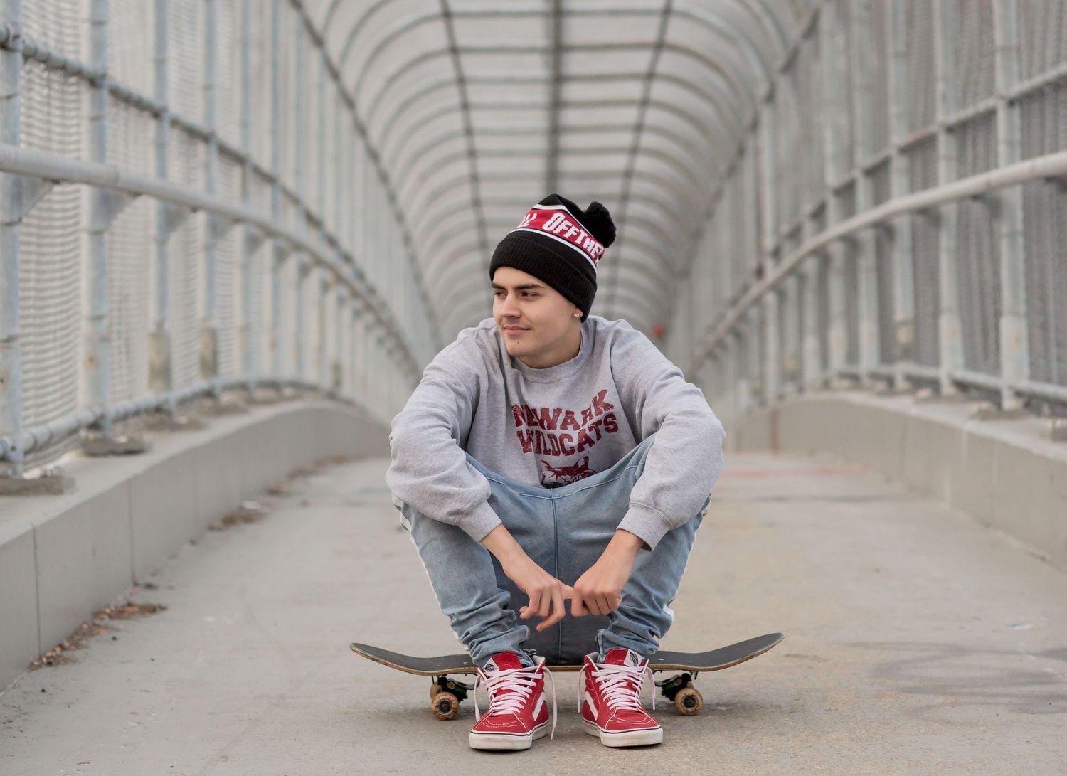 Young male skateboarder crouching on skateboard inside a modern pedestrian bridge tunnel.