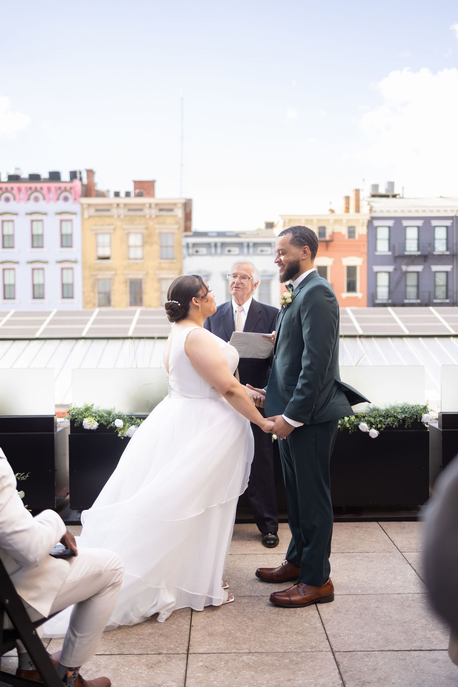 Couple exchanges vows on a rooftop wedding ceremony with colorful city buildings in the background at The Columns in Cincinnati's OTR.