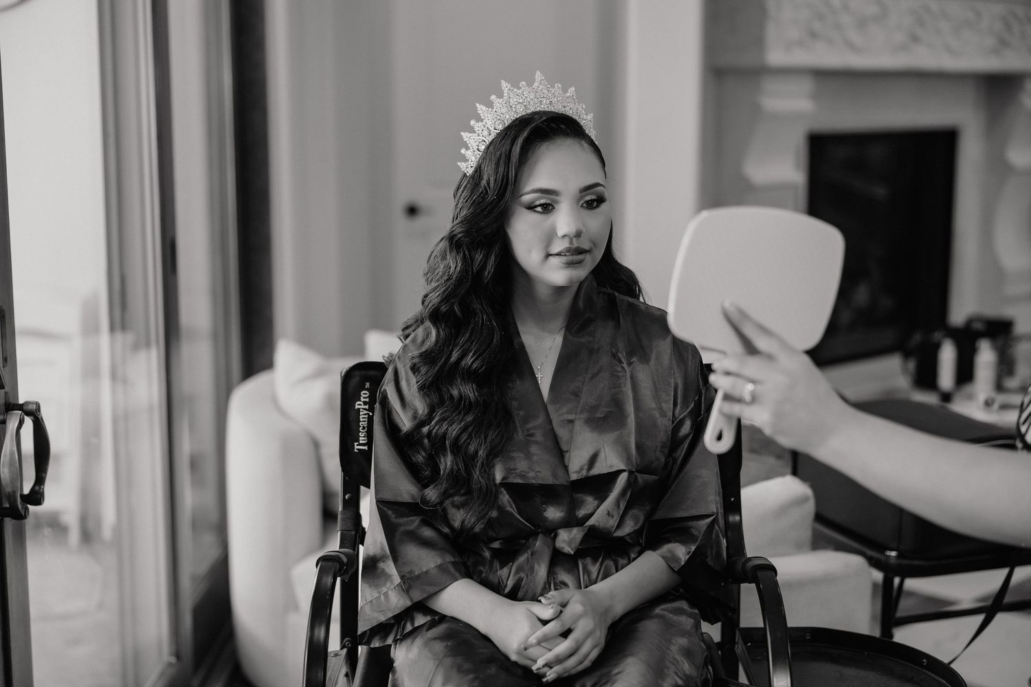 A bride-to-be wearing a crown tries on her look while seated in a wheelchair during wedding preparations.