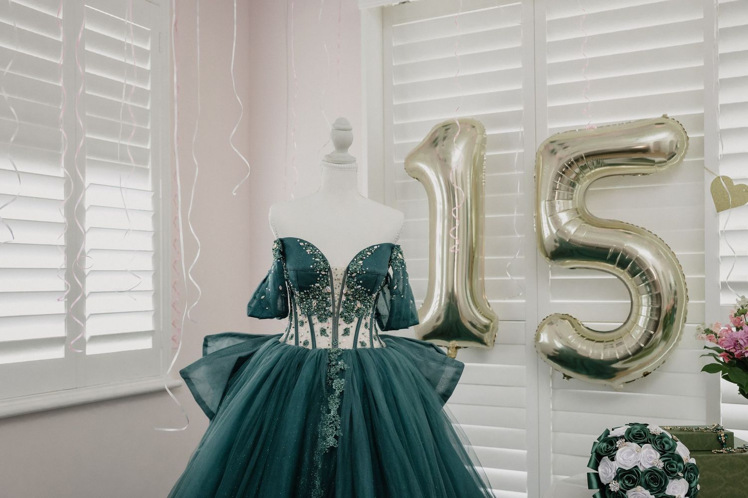 Elegant green quinceañera ball gown displayed on a mannequin with gold number 15 balloons for a birthday celebration.
