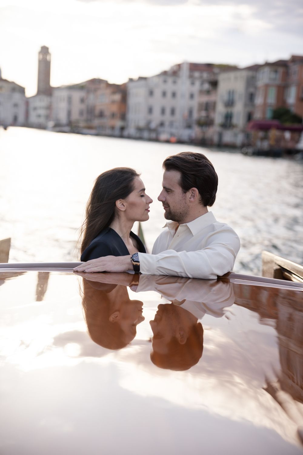 Romantic couple embracing on a wooden boat in Venice canal with historic buildings in the background.
