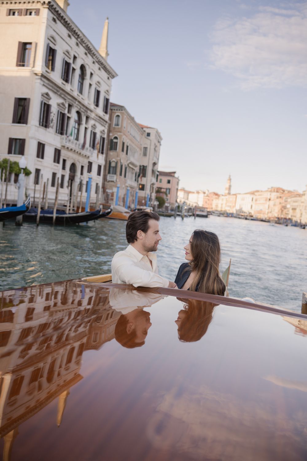 Romantic couple sharing an intimate moment on a wooden boat along Venice Grand Canal with historic buildings backdrop.