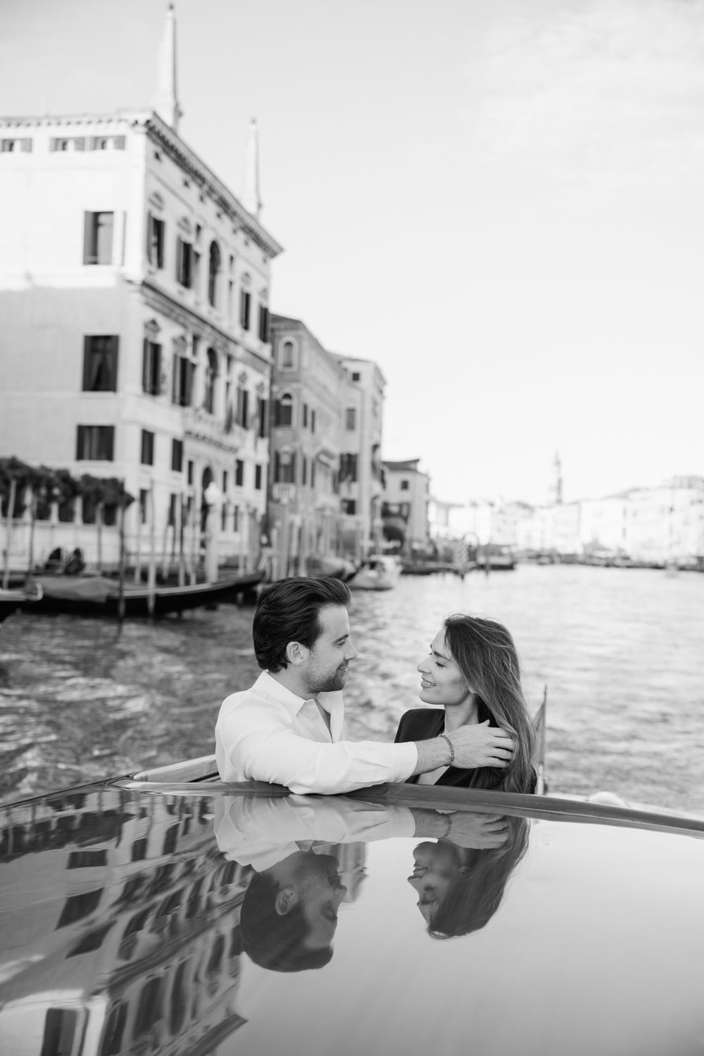 Black and white photo of a romantic couple embracing on a boat along the Grand Canal in Venice, Italy.