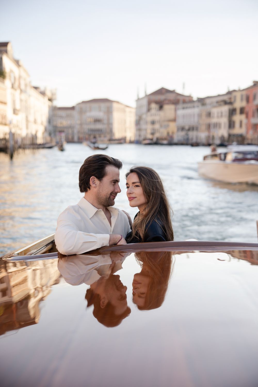 Romantic couple sharing an intimate moment on a boat along Venice's Grand Canal with colorful buildings in background.