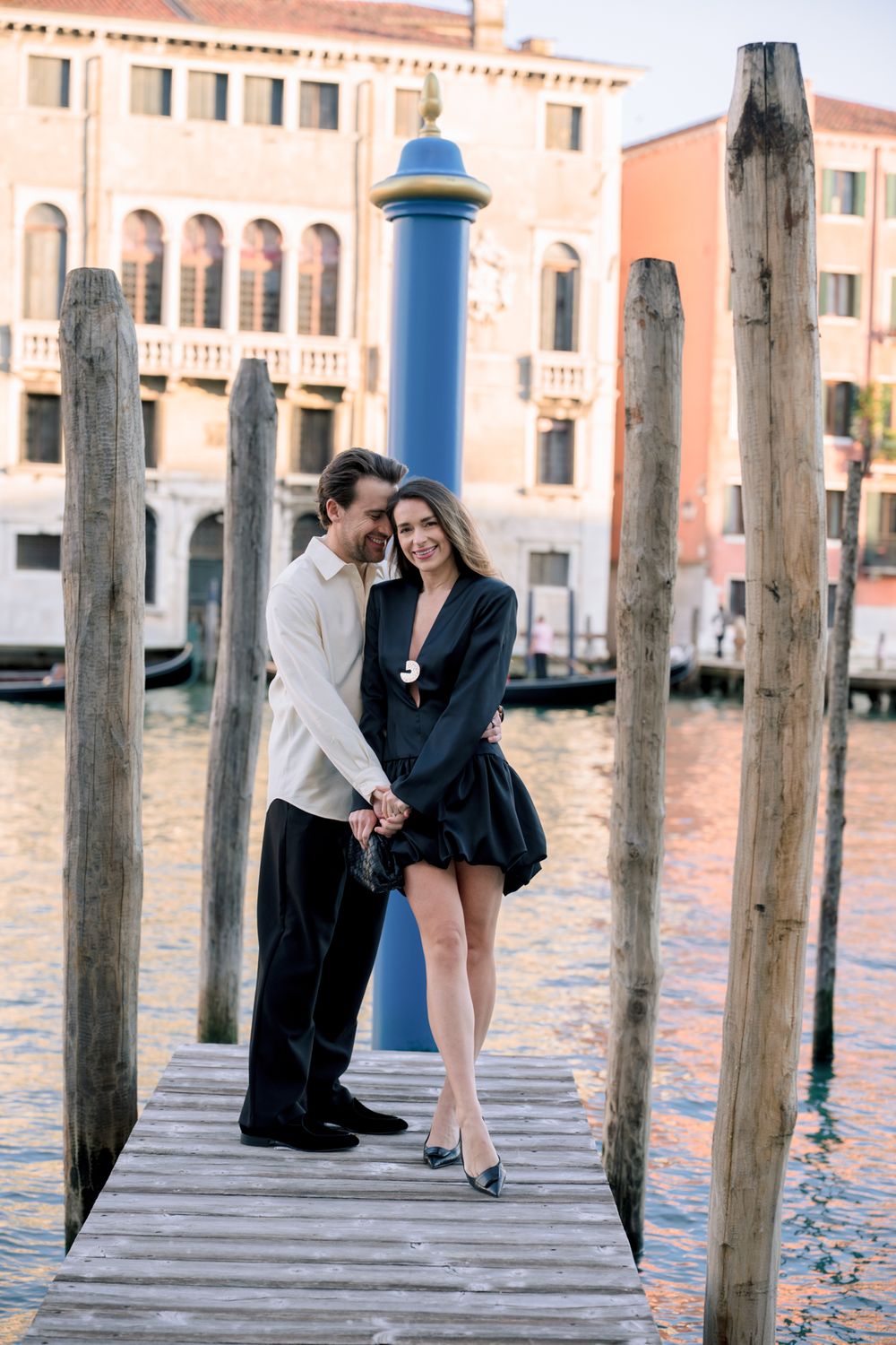 Romantic couple embracing on a wooden dock in Venice, Italy, with the Grand Canal and historic buildings at sunset.