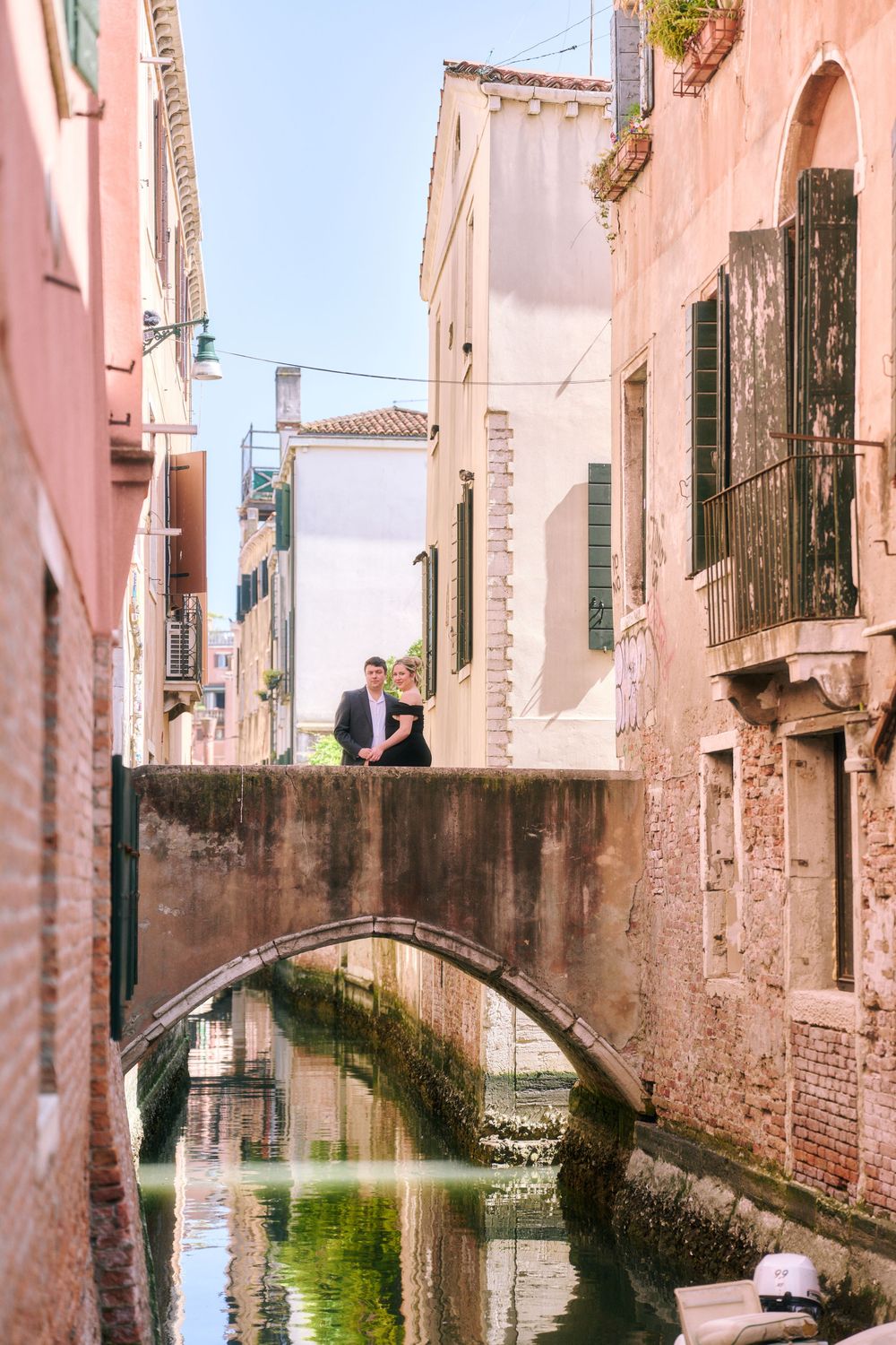 Couple standing on a charming stone bridge over a Venice canal, surrounded by colorful historic buildings.