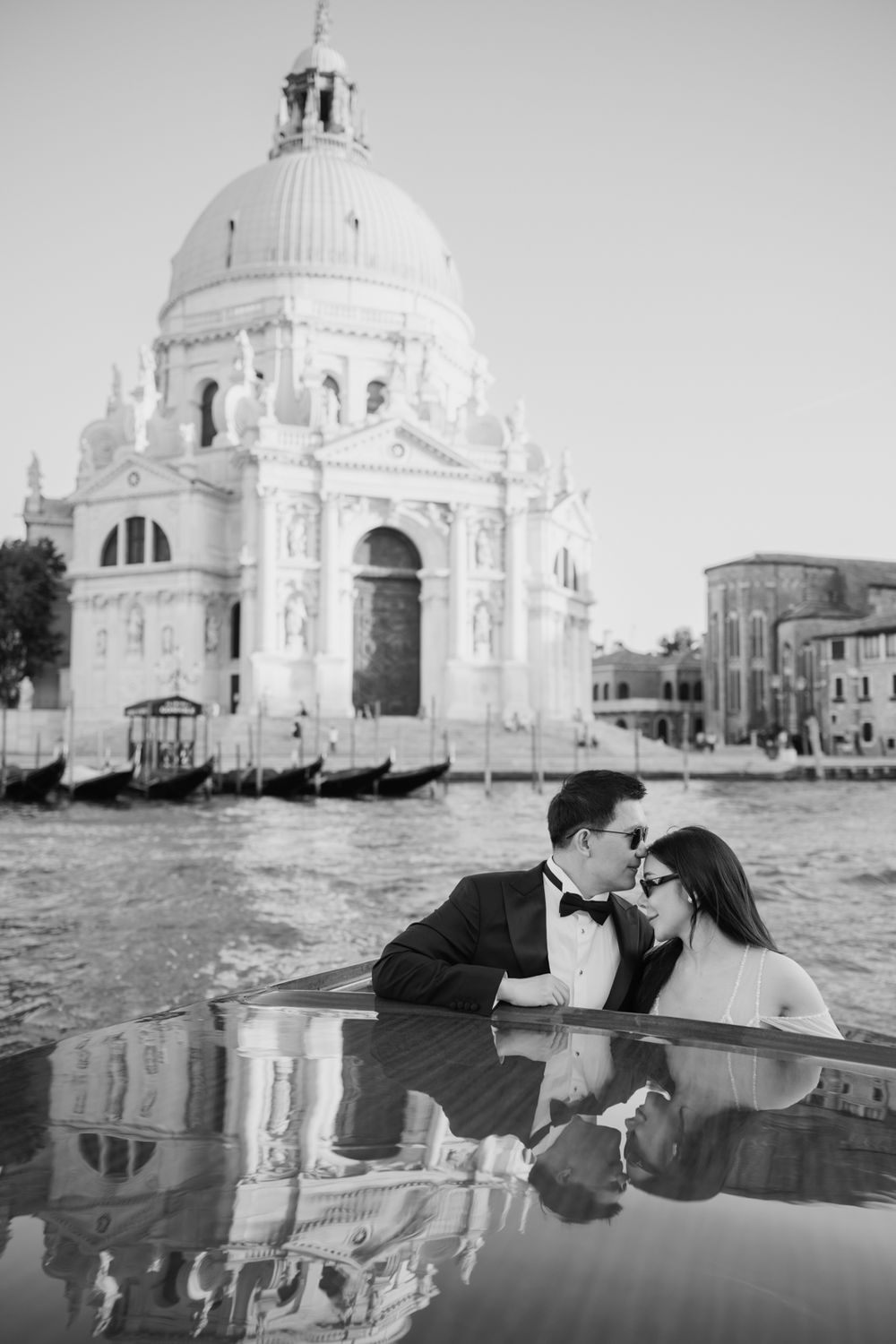 Couple in formal attire sharing a romantic moment on a boat with Santa Maria della Salute basilica in Venice.
