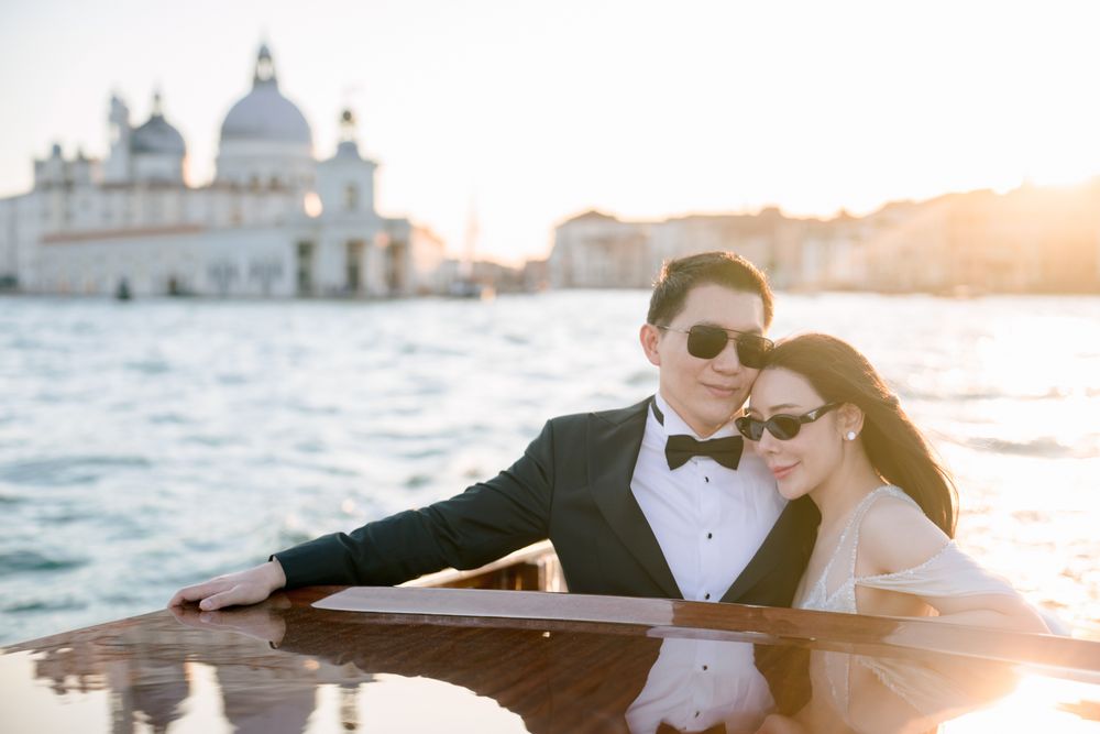 Couple in formal wear posing on a wooden boat in Venice with Santa Maria della Salute at golden hour.