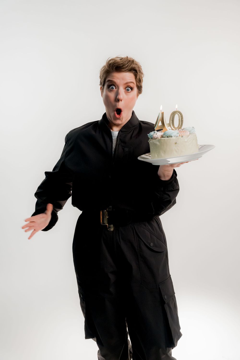 Shocked person in black coat holding a 40th birthday cake with lit candles on white background.