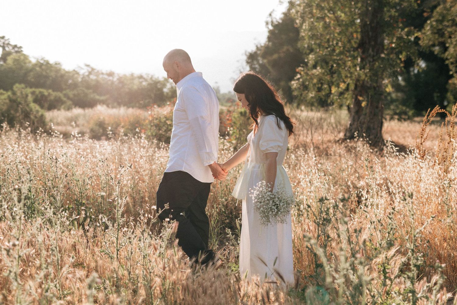 A couple walks through Ojai fields at golden hour for wedding photos on film photography.