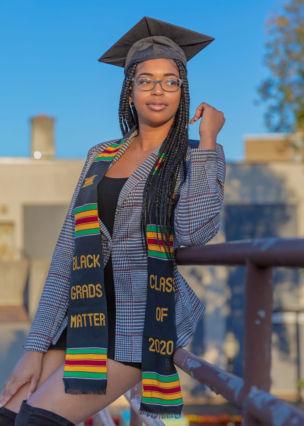 Graduate in academic regalia and patterned stole poses outdoors on graduation day.