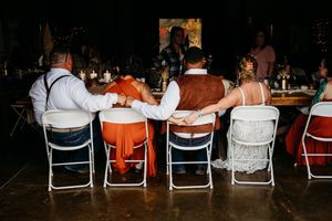 Bride and groom holding hands with wedding party at sweetheart table during rustic barn reception.