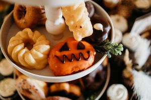 Halloween themed dessert display with jack-o-lantern cookie, mini donuts, and chocolate treats on a tiered stand.