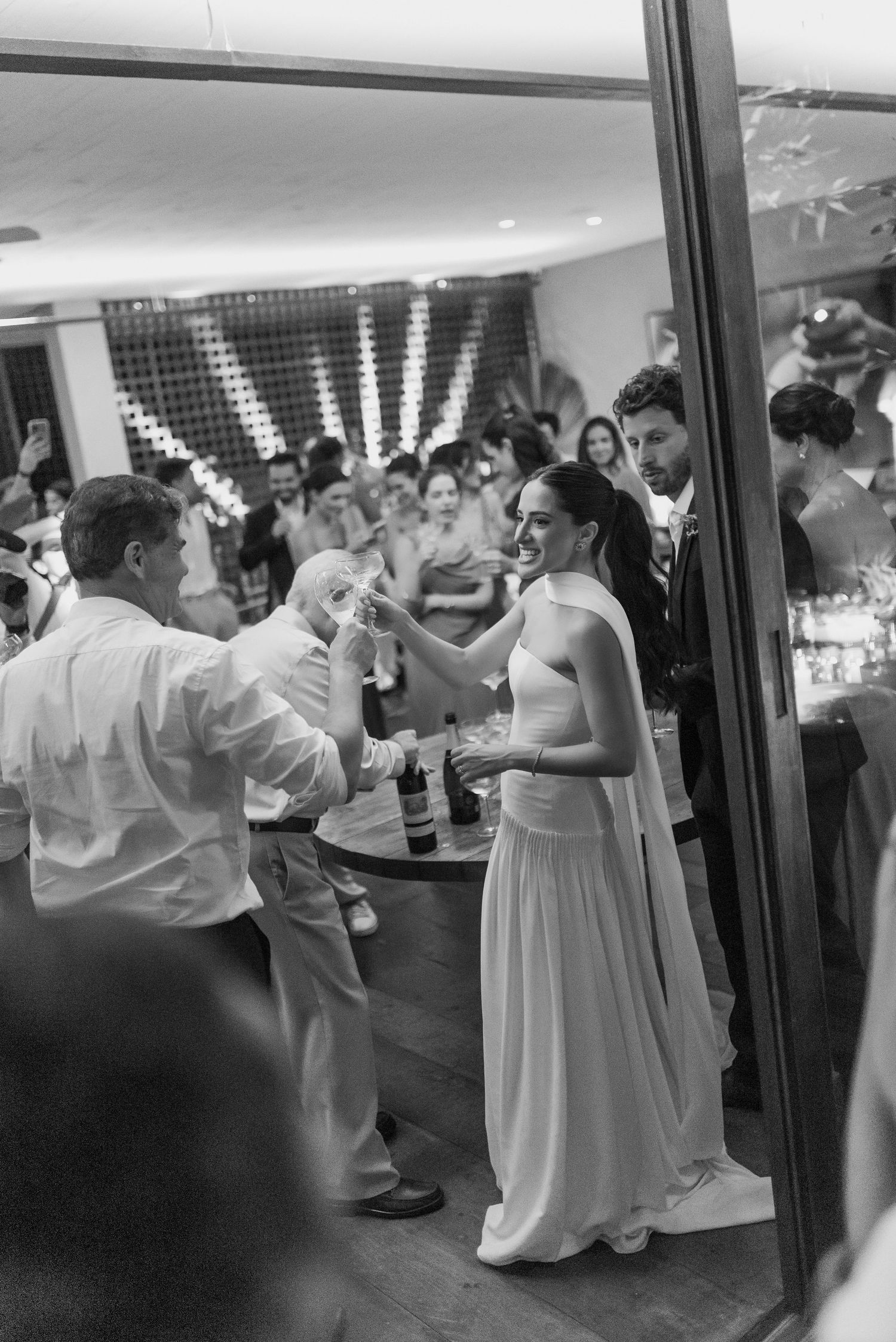 Bride in white halter gown toasting with guests at elegant wedding reception in black and white.