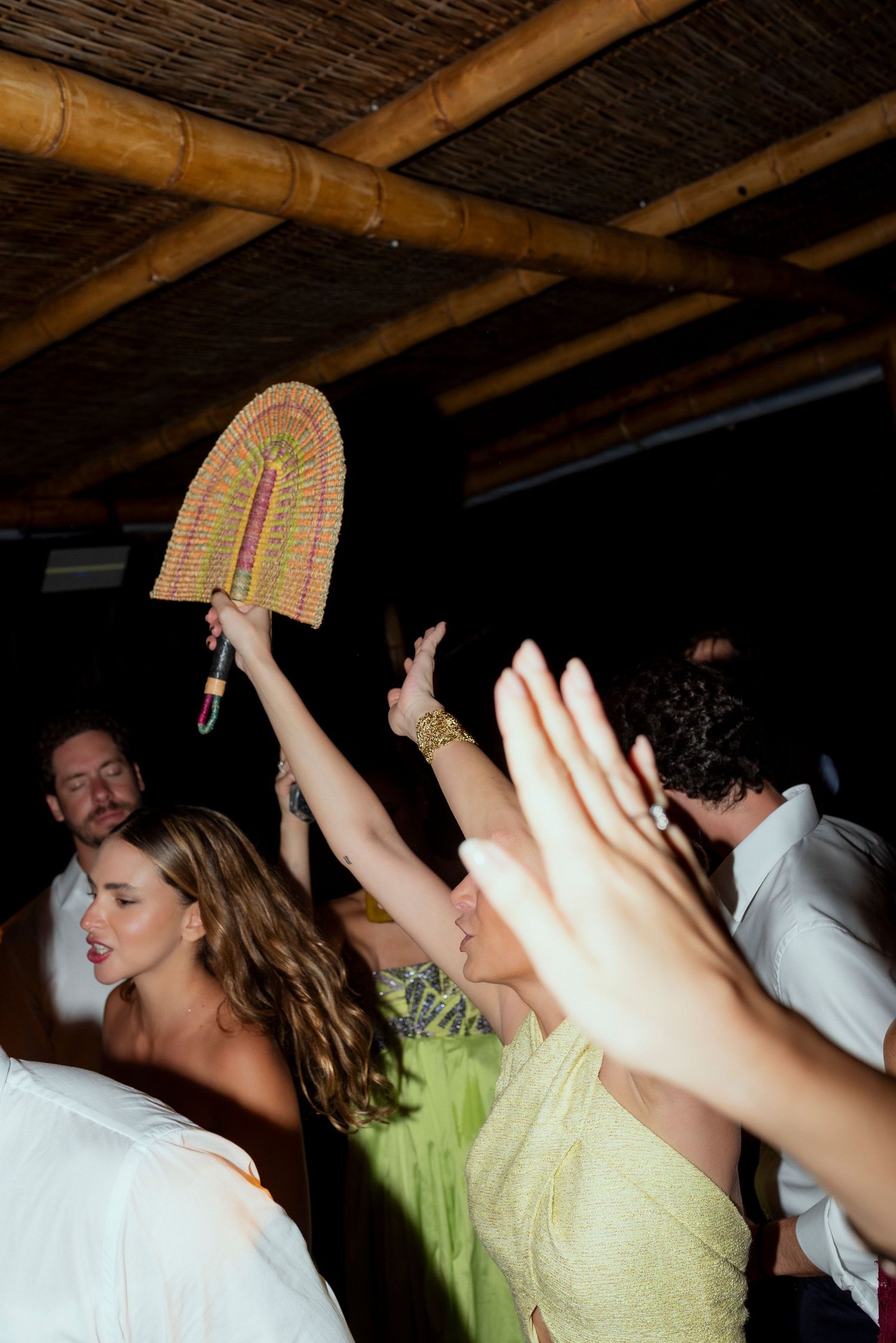 Guests dancing and celebrating at a tropical wedding reception under a bamboo ceiling.