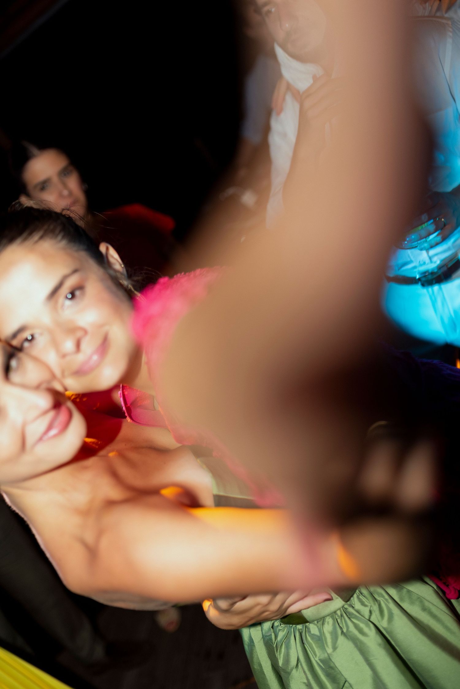 Women dancing and smiling at a vibrant nightclub party with colorful lights and festive atmosphere.
