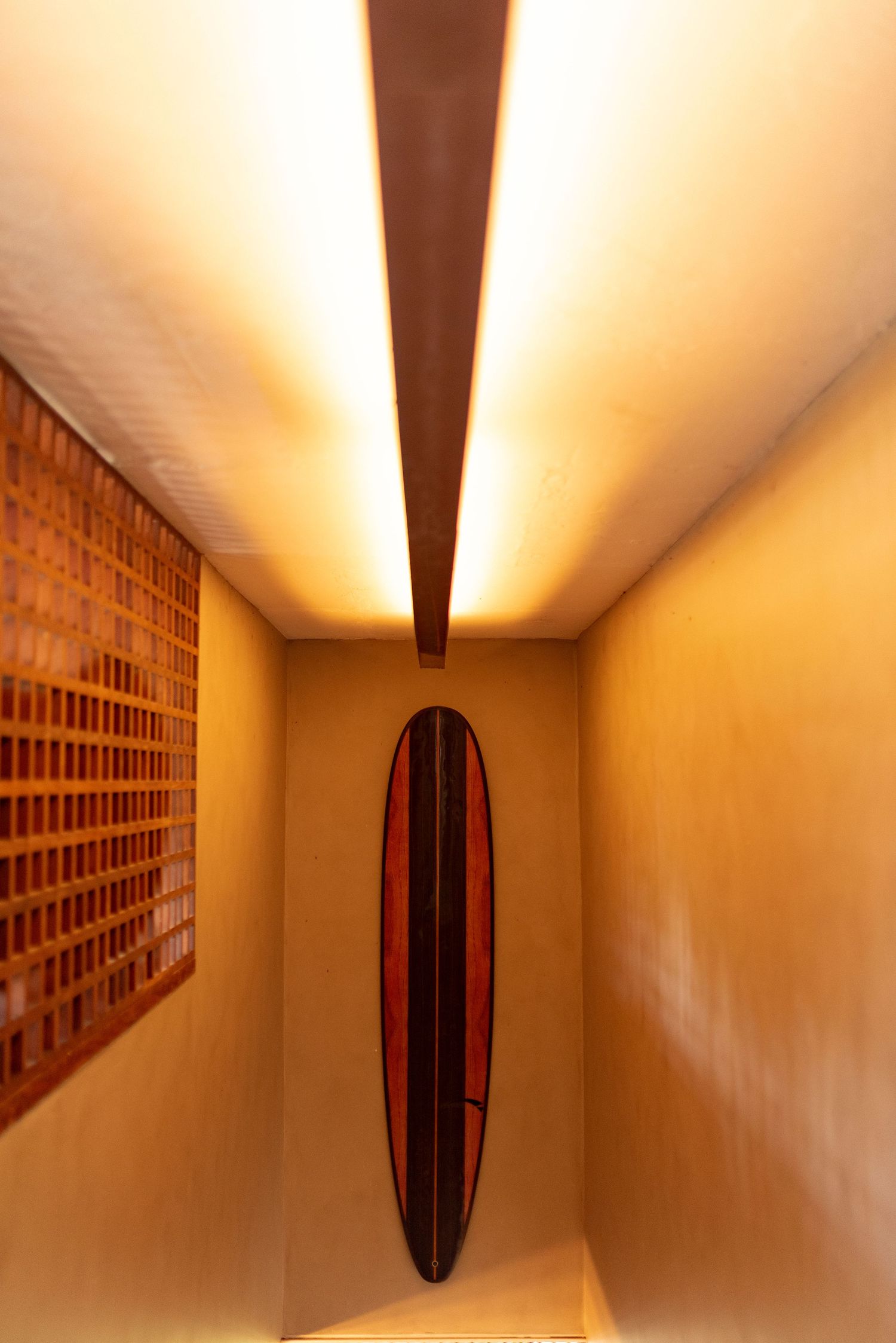 Warm-lit narrow hallway with a decorative surfboard mounted on the wall and a brick art panel beside it.