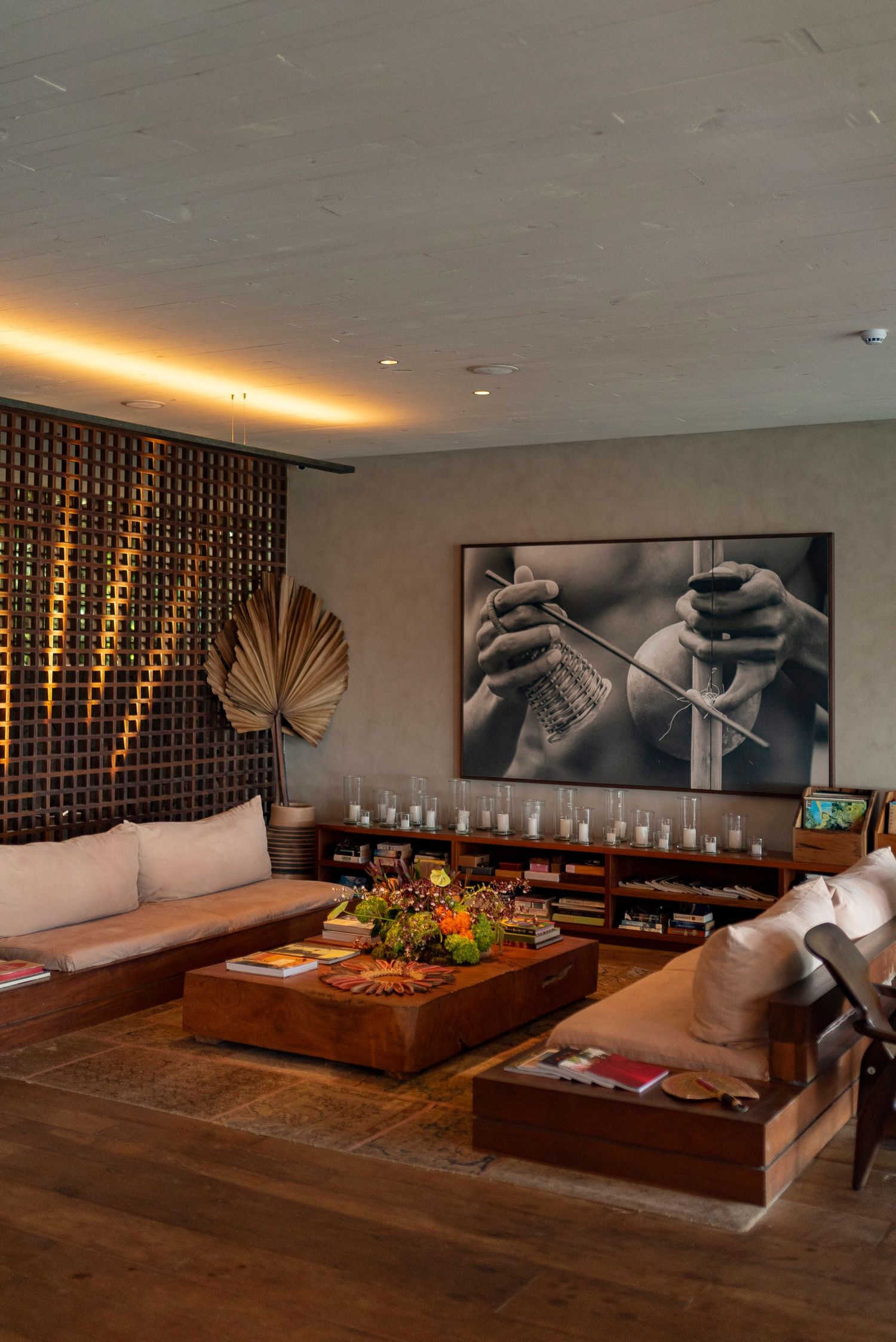 Stylish lounge with wooden sofas, candles, coffee table, large black-and-white art, and warm ambient lighting.