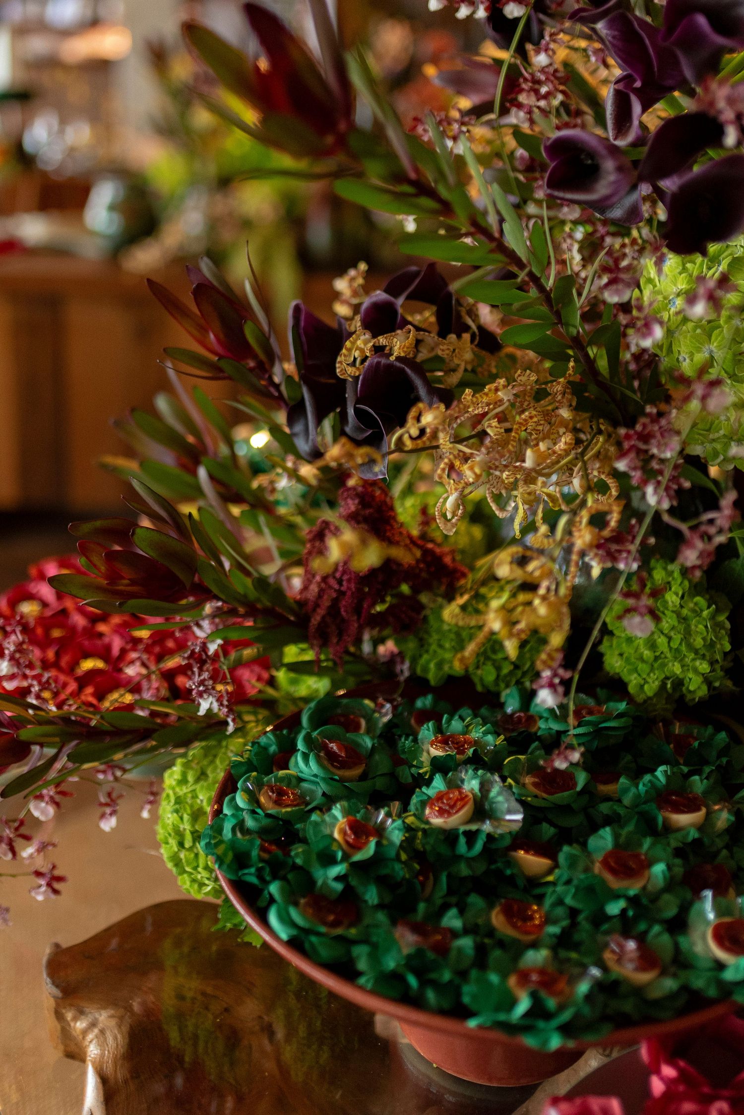 Lush floral arrangement with dark calla lilies, red blooms, and green cupcakes on a decorative tiered display.