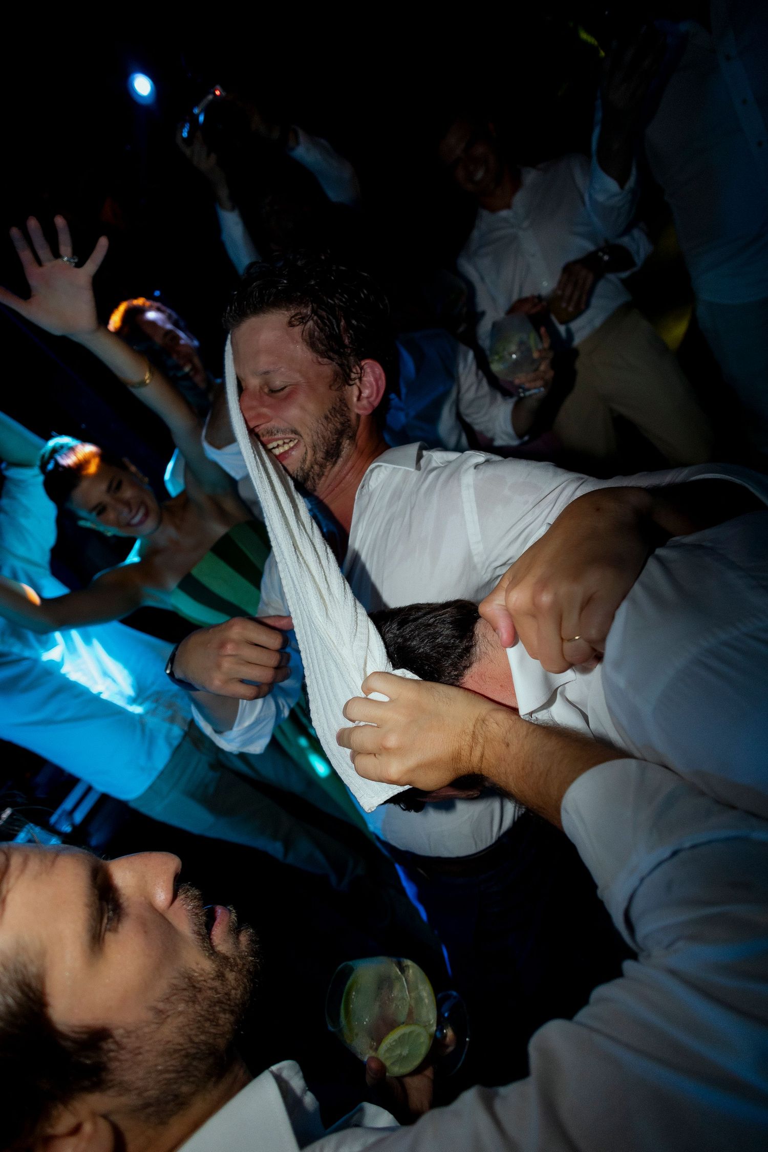 Men celebrating at a lively nighttime party, laughing and dancing together under blue lights.