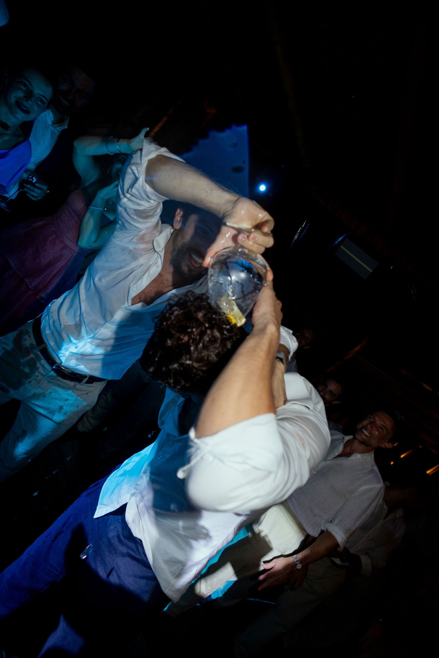 People partying at a nightclub, with one person drinking from a bottle held by another in a lively crowd.