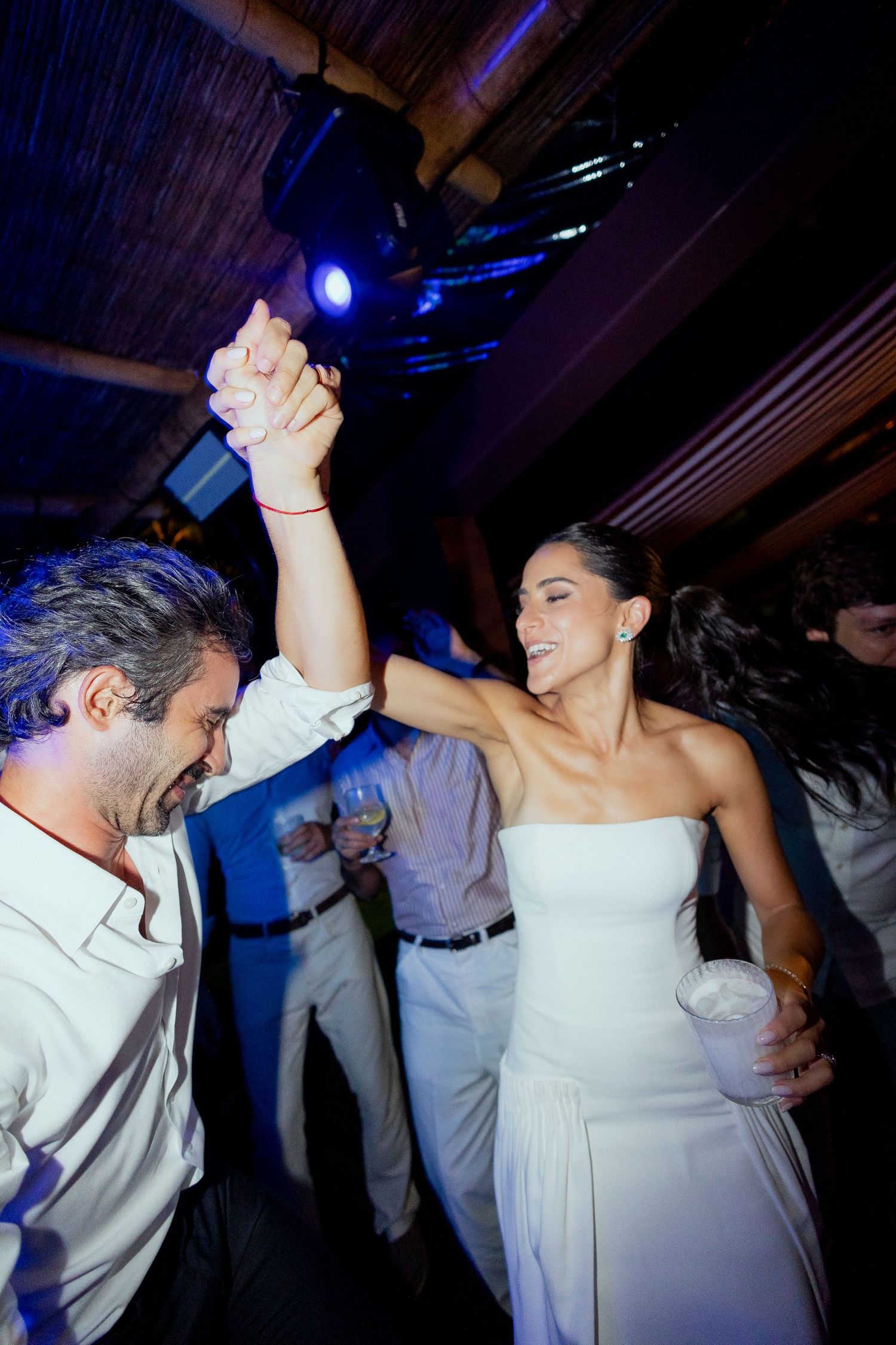 Bride and groom dancing joyfully at their wedding reception, holding hands under blue lights.
