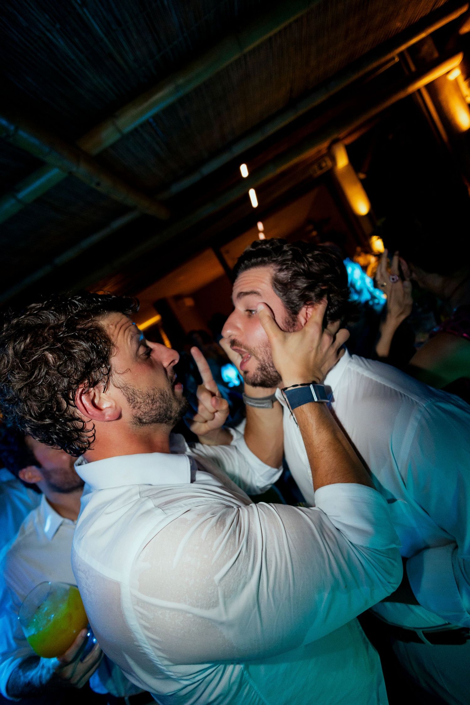 Two men in white shirts dancing closely together at a lively party or wedding reception event.