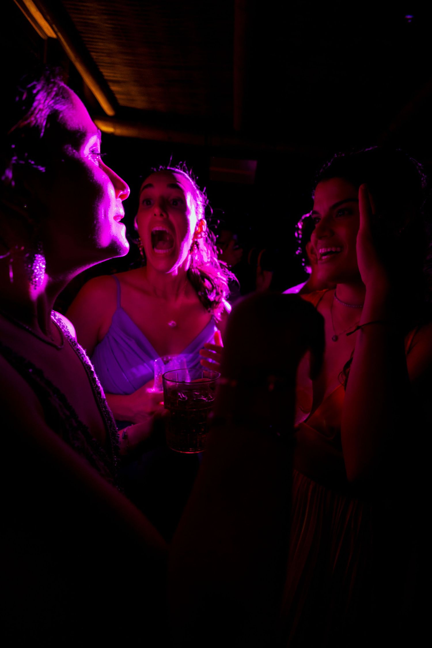Group of friends dancing and laughing under vibrant pink party lights at a nightclub event.