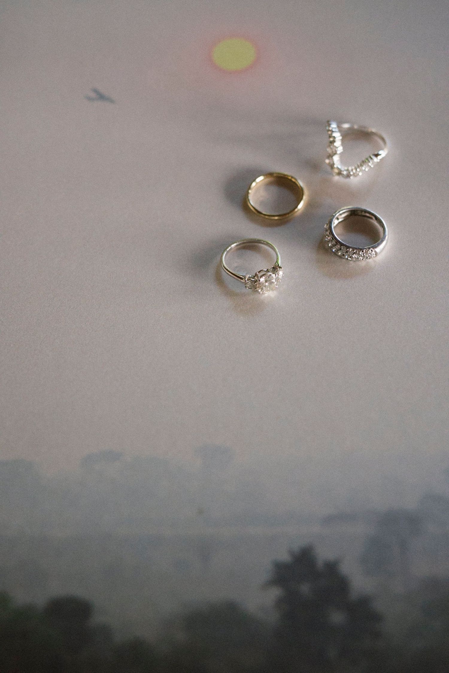 Four wedding rings displayed on a misty window surface, including diamond engagement rings and gold bands.