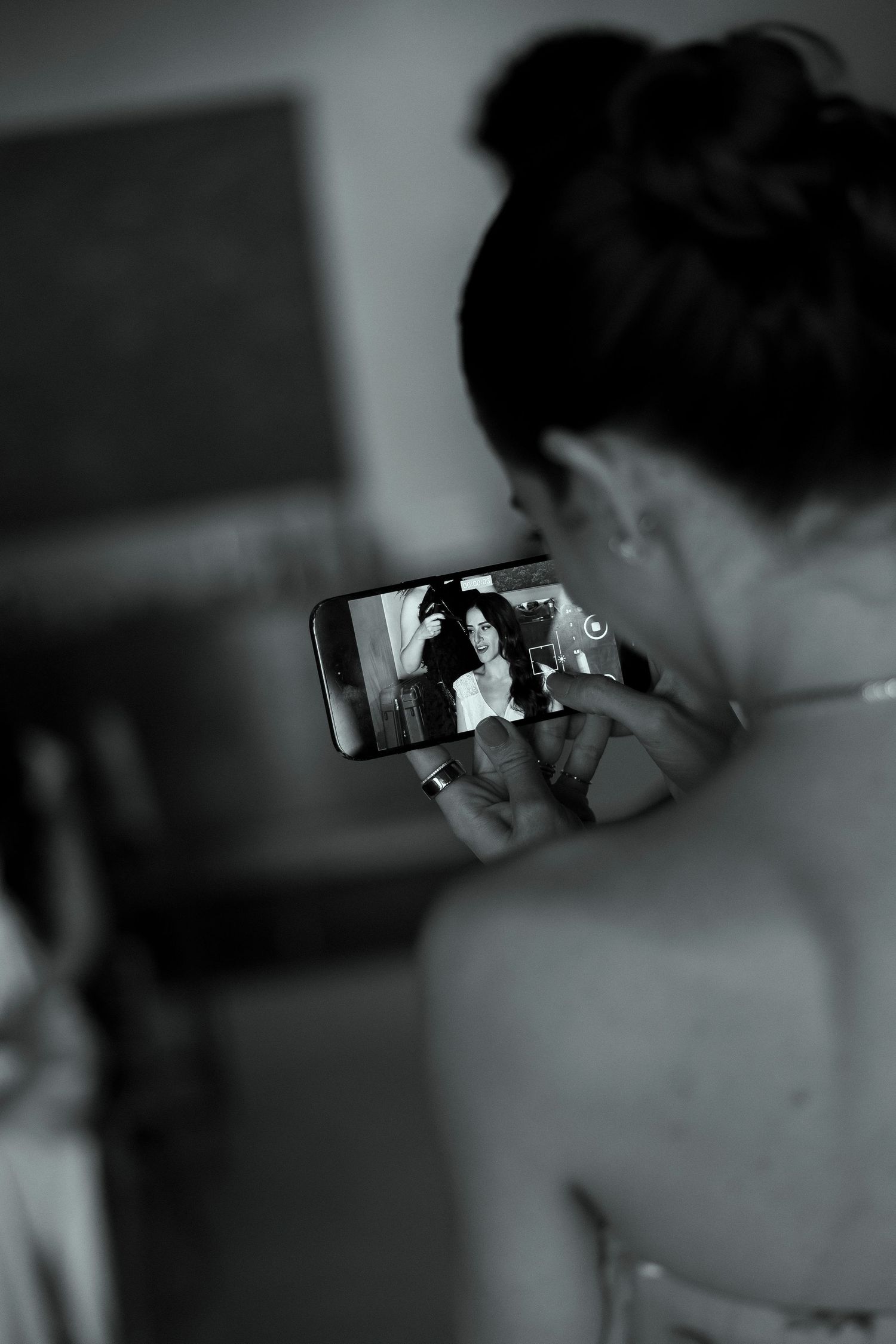 Black and white photo of a woman taking a selfie on her smartphone, capturing her reflection in a mirror.