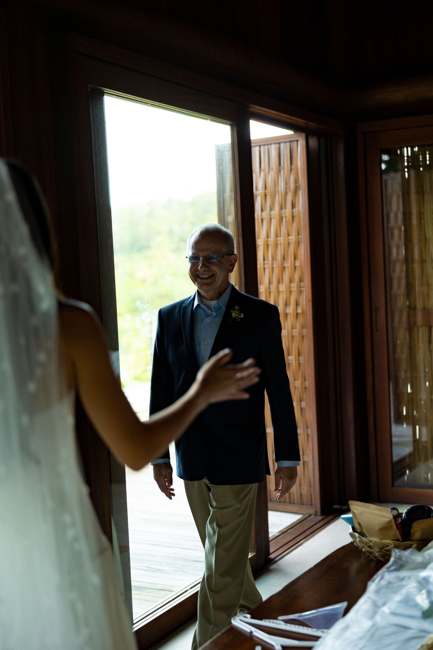 A smiling father in a navy blazer sees his bride daughter for the first time on her wedding day.