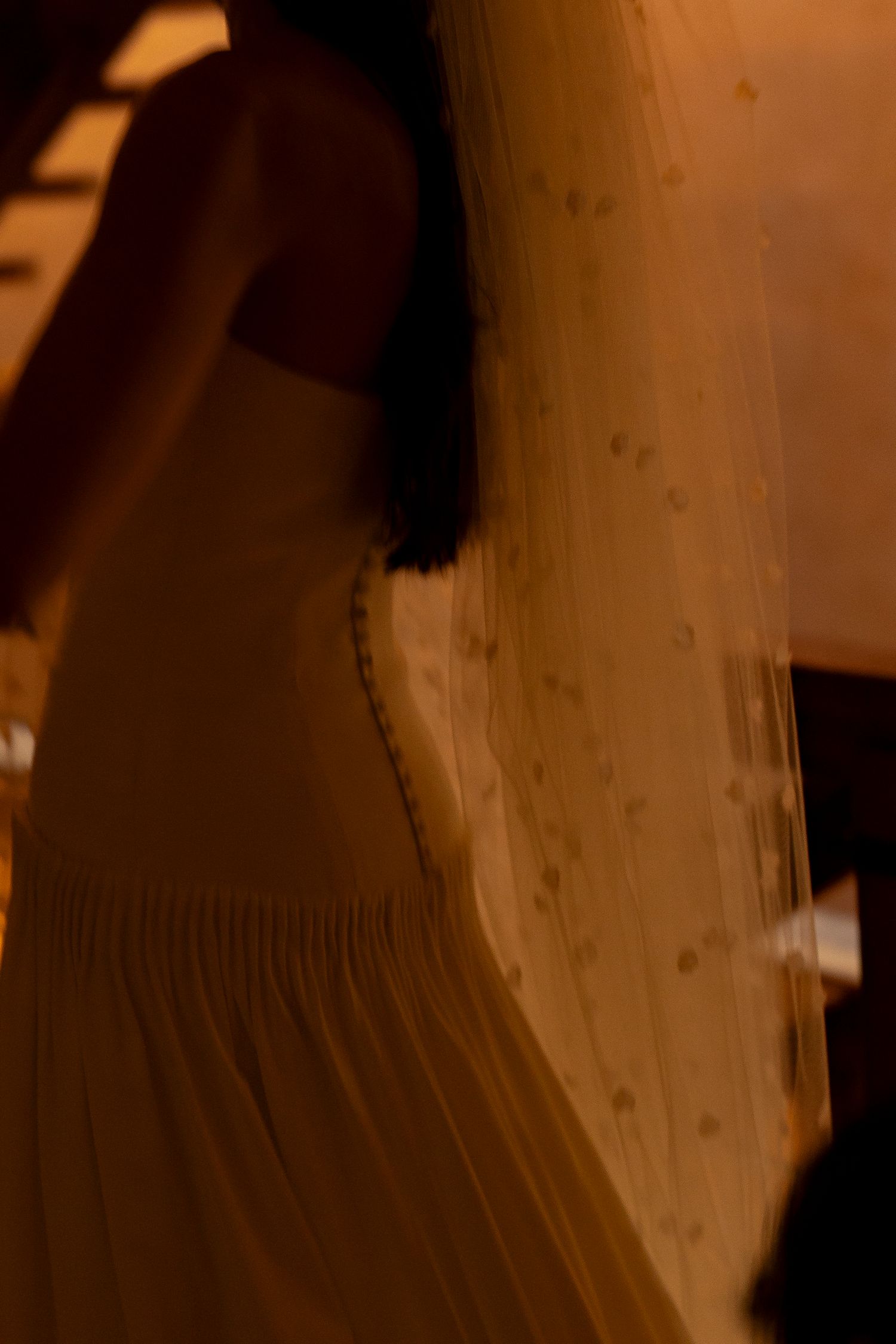 Blurred motion shot of a bride in a white wedding dress with a dotted veil under warm amber lighting.