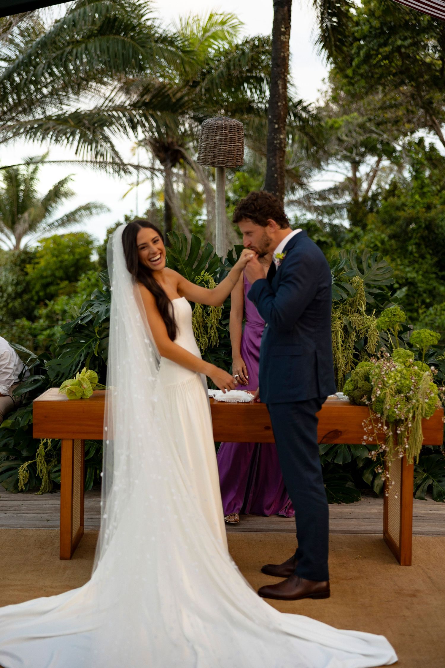 Bride and groom exchange rings outdoors at a tropical wedding ceremony surrounded by lush greenery.