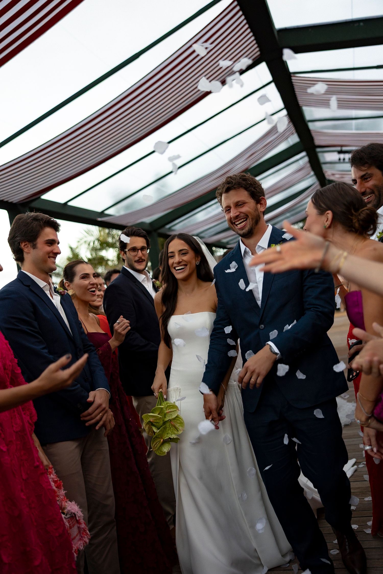 Joyful bride and groom walk through confetti shower surrounded by cheering guests at elegant outdoor wedding ceremony.