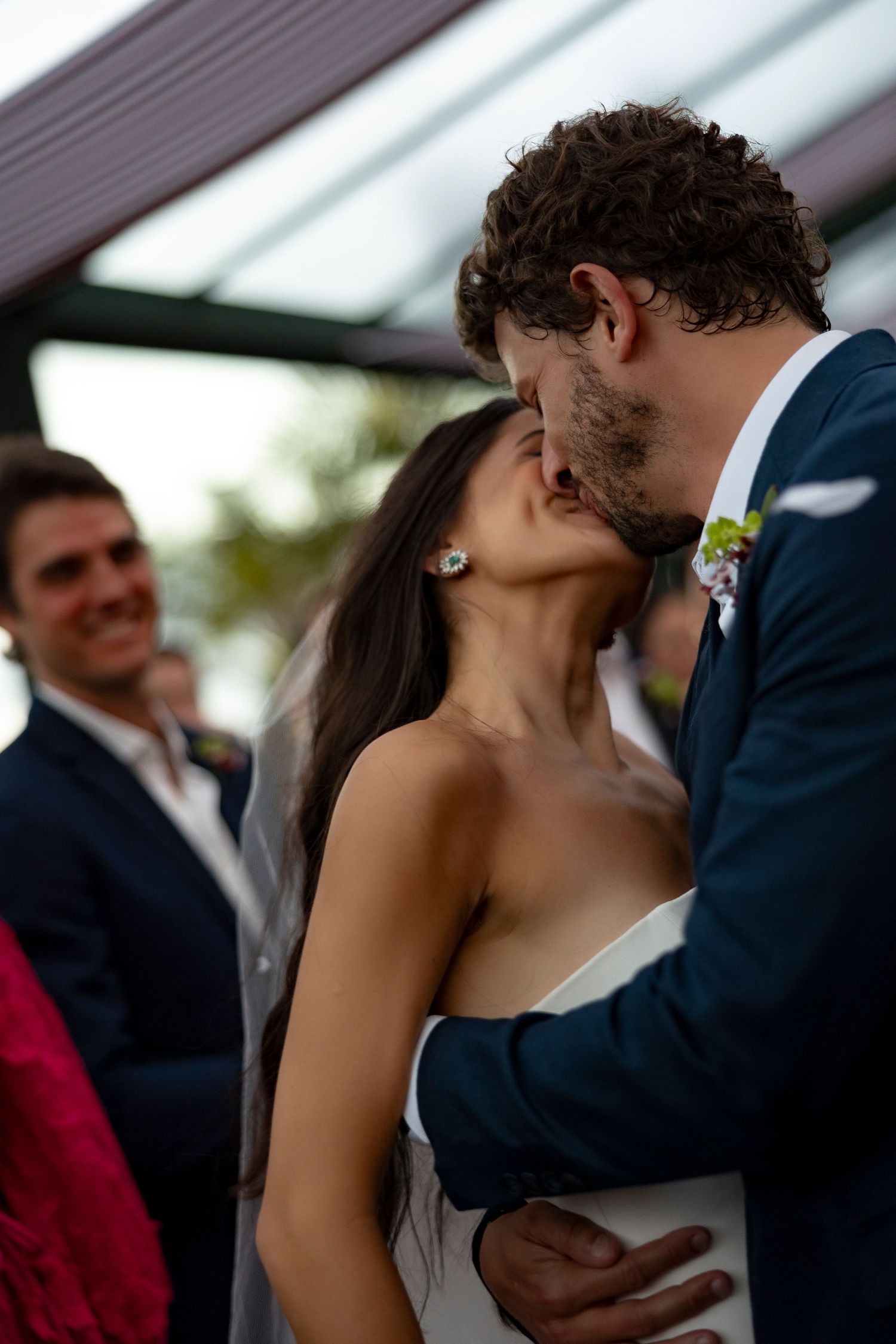 Bride and groom share their first kiss at wedding ceremony while guests smile in background.