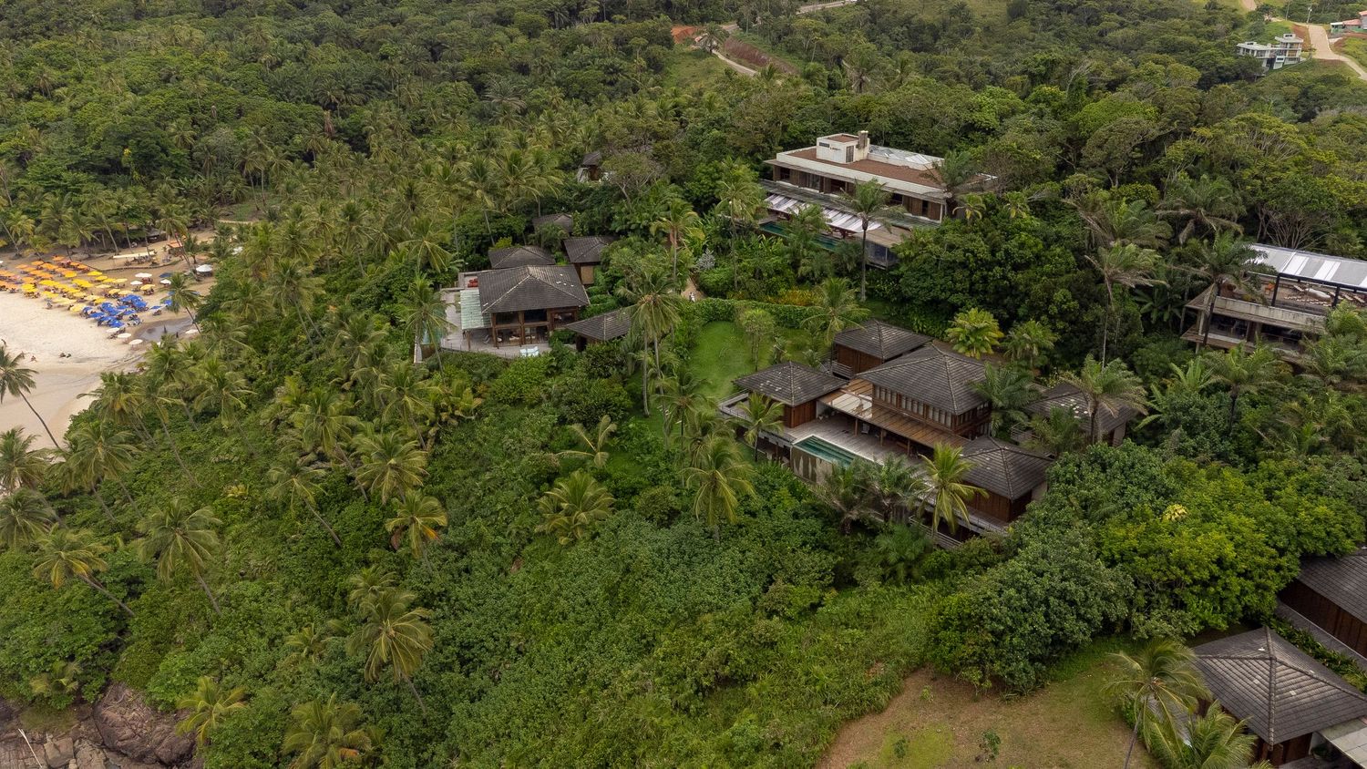 Aerial view of tropical resort nestled among lush palm trees near a sandy beach in a dense green jungle setting.
