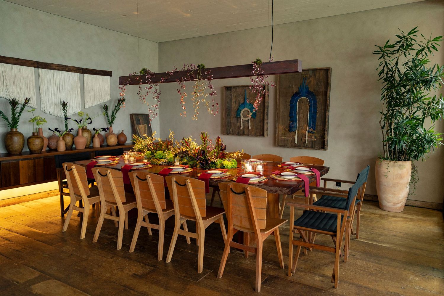 Elegant dining room with long wooden table, rattan chairs, floral centerpieces, and hanging greenery chandelier.