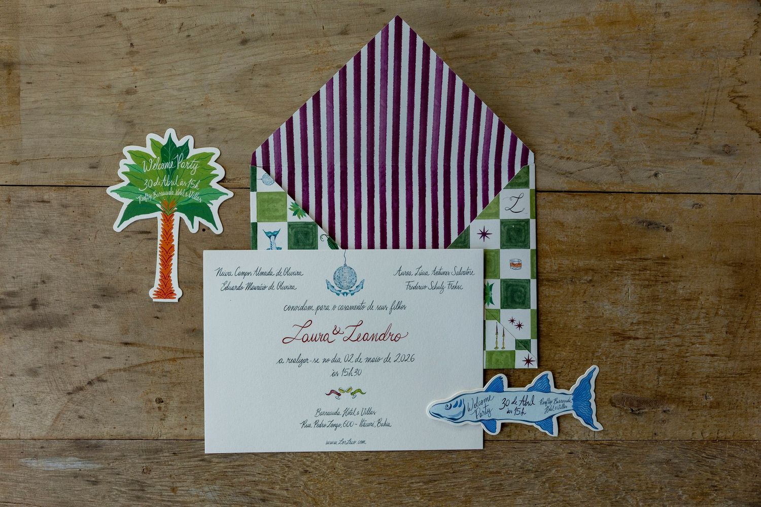 Elegant wedding invitation with fish and palm tree accents, striped purple envelope liner on rustic wood background.