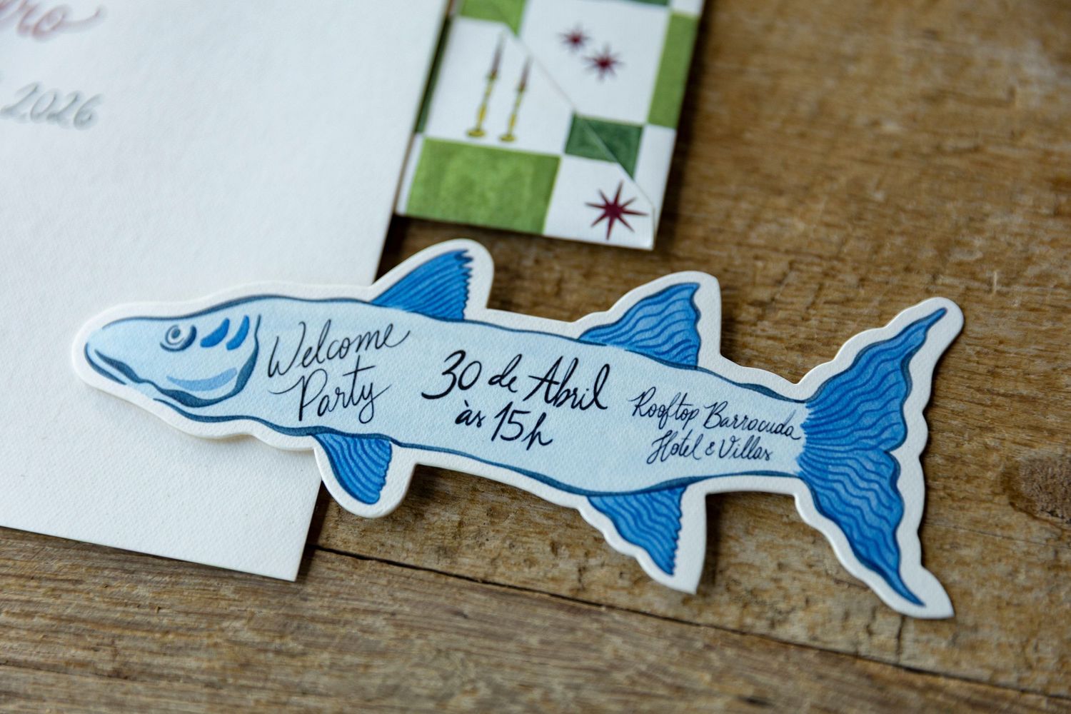 Blue barracuda fish-shaped party invitation card with handwritten text reading Welcome Party 30 de Abril.