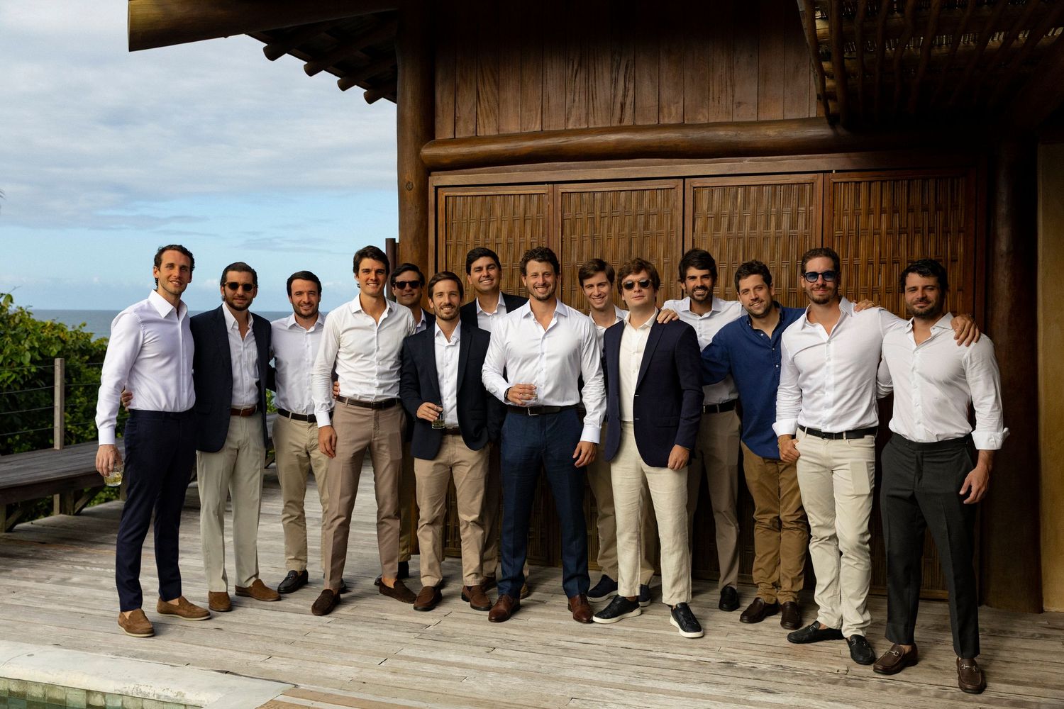 Group of young men in smart casual attire posing together on a wooden deck with scenic views.