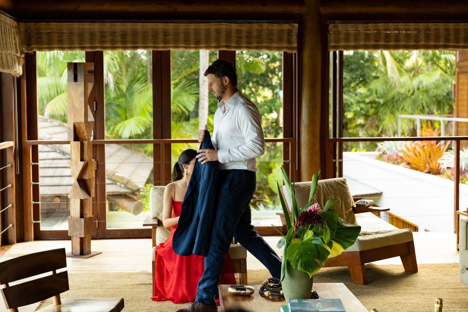 Couple dancing in an open-air tropical villa with lush green palm trees and wooden architecture.