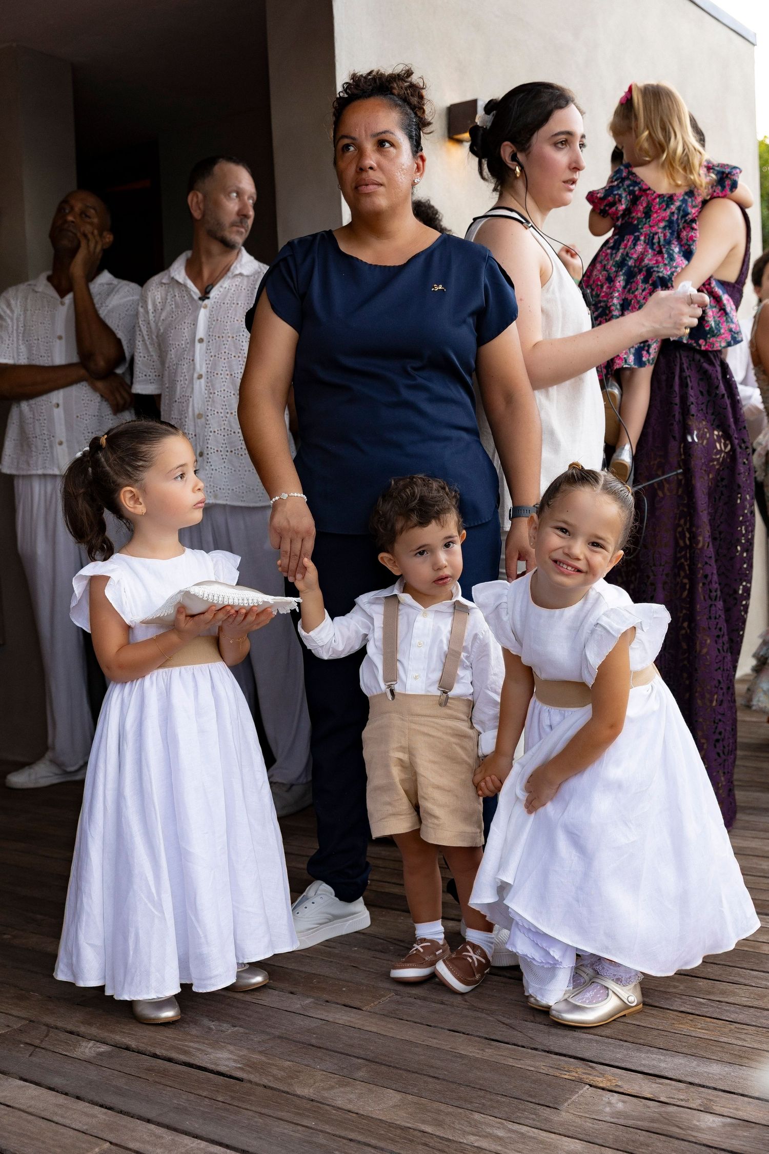 Woman in navy top with three children in white formal attire at an outdoor wedding celebration.