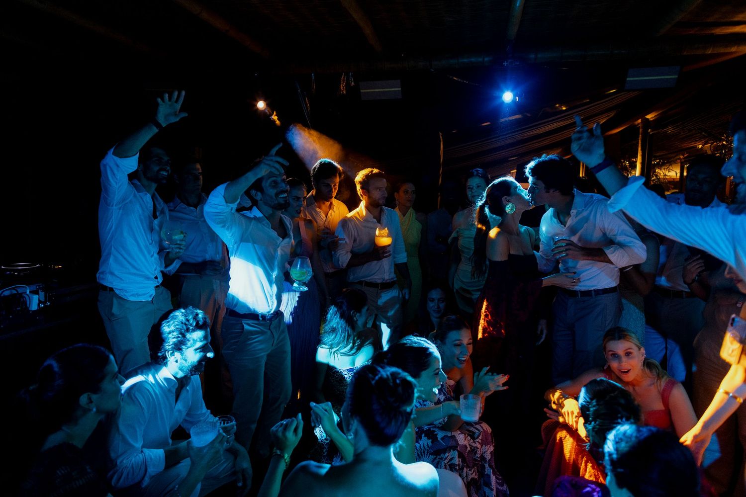 Crowd of people dancing under blue and teal lights at a lively indoor party or nightclub event.