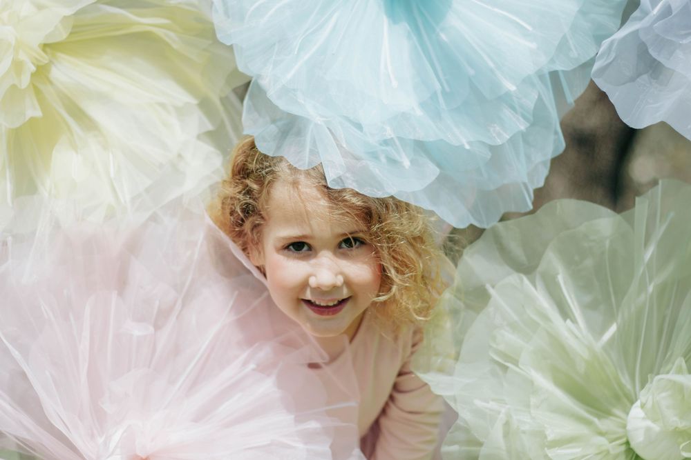 Smiling curly-haired girl surrounded by pastel tulle pom-poms in pink, yellow, and mint green.