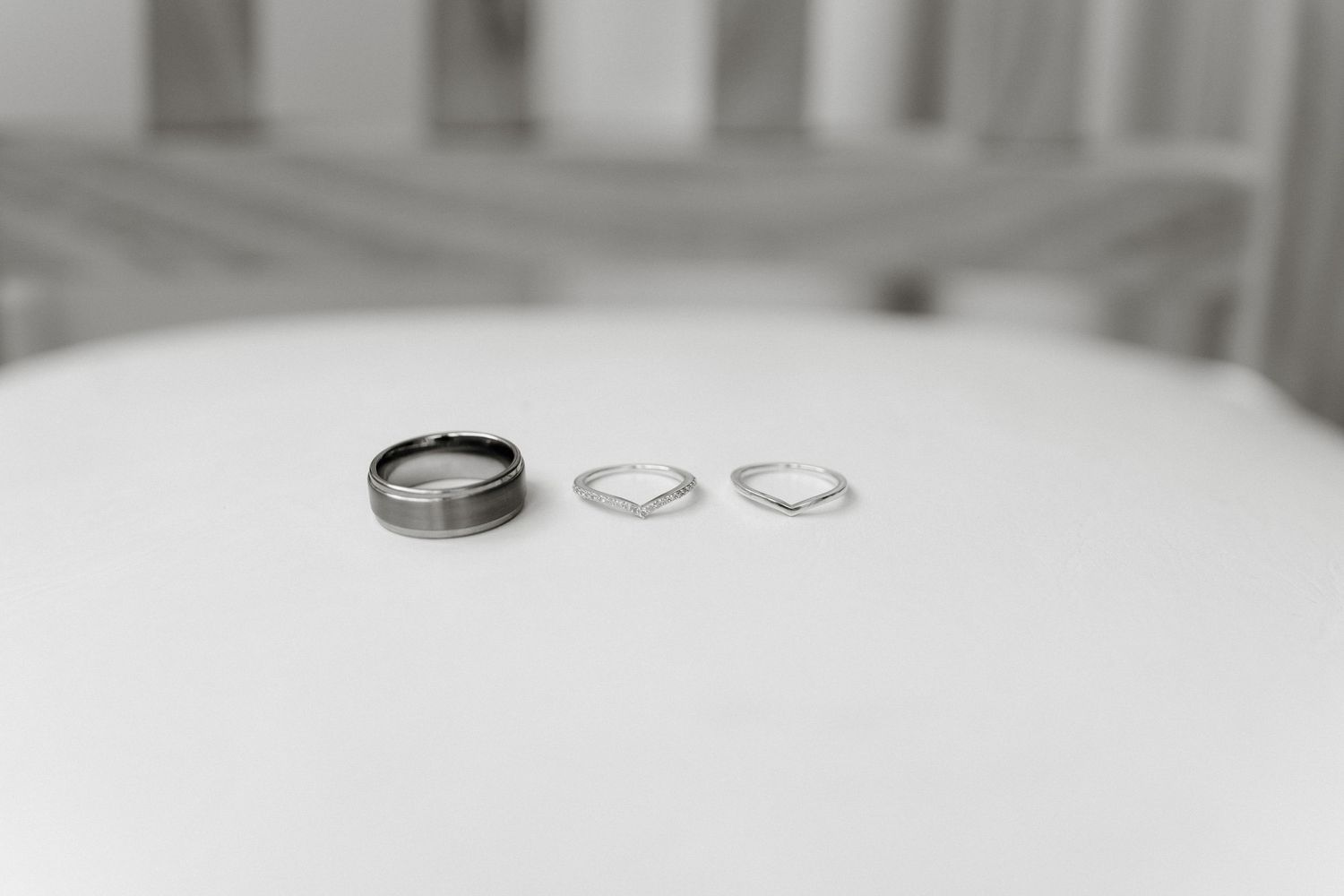 Three wedding rings on a white surface, including a wide tungsten band and two delicate silver chevron rings.