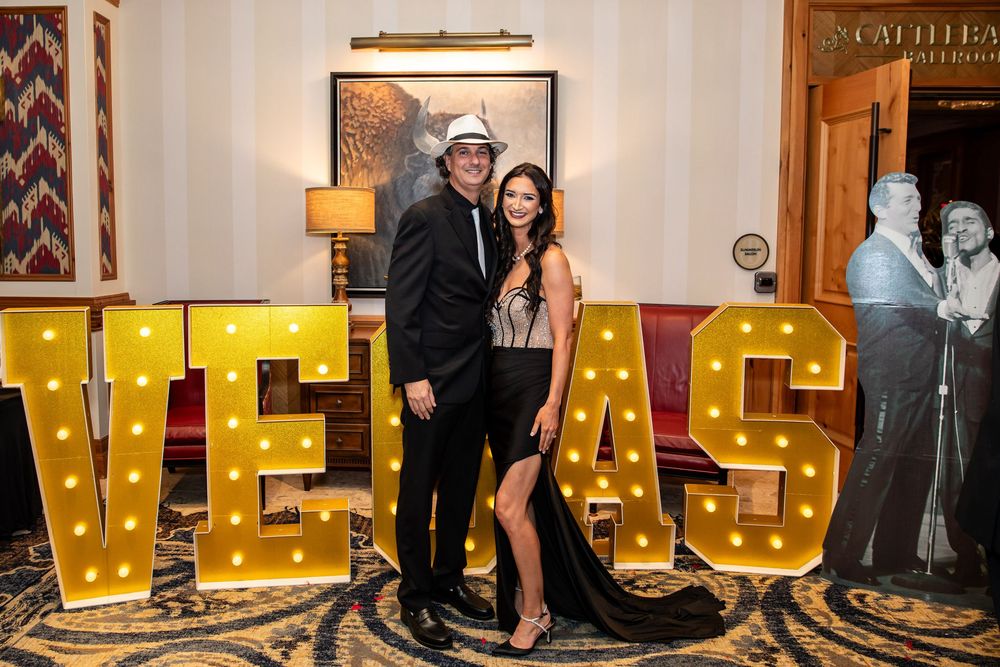 Couple posing in front of illuminated VEGAS marquee letters at a glamorous Las Vegas themed event.