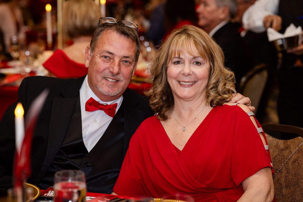 Couple in red formal attire smiling at a gala dinner event, man in bow tie, woman in red dress.