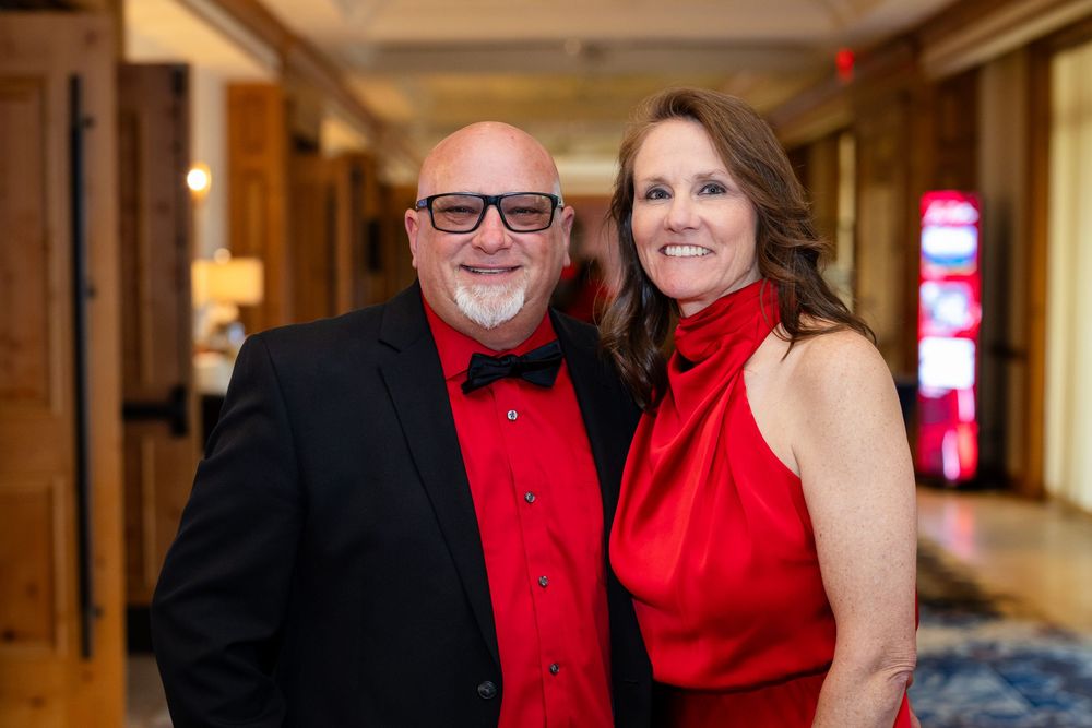 Couple in matching red outfits smiling at a formal event in an elegant hotel hallway.